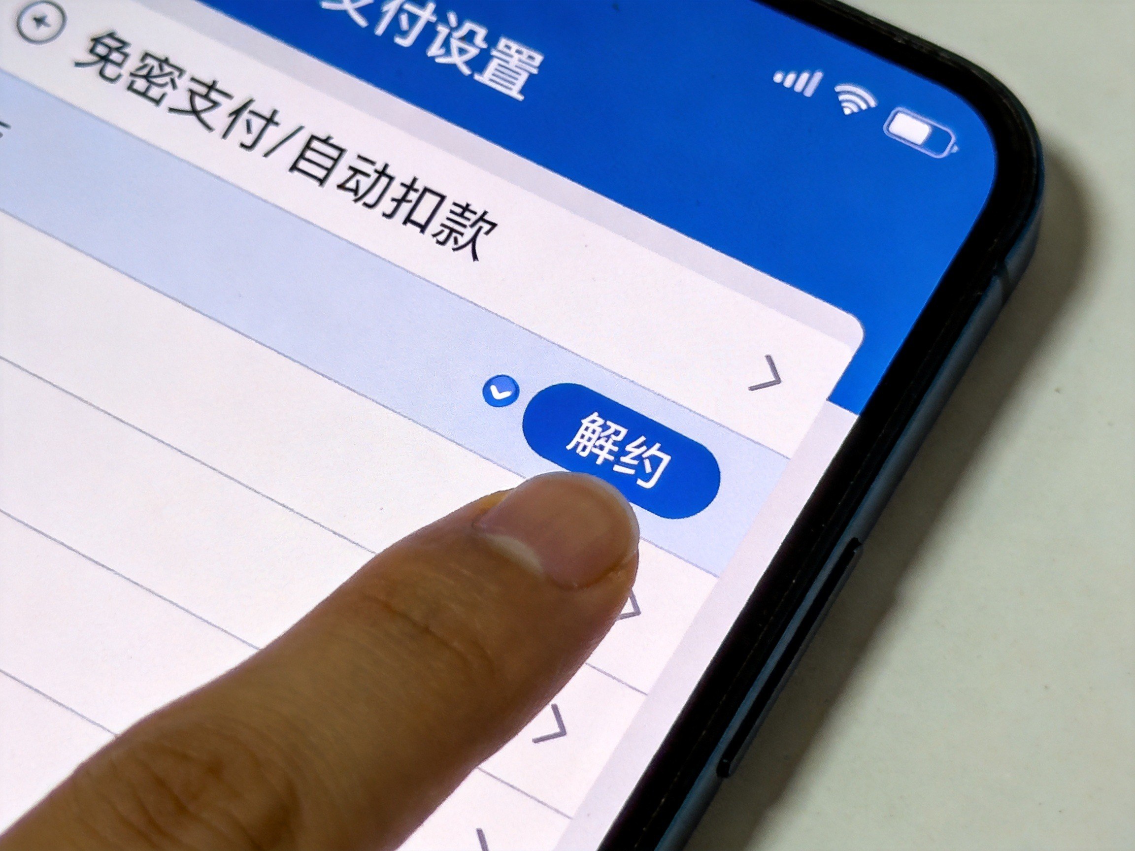 GEO正文图二：手机屏幕显示支付宝支付设置中的免密支付/自动扣款界面，手指正在点击解约按钮