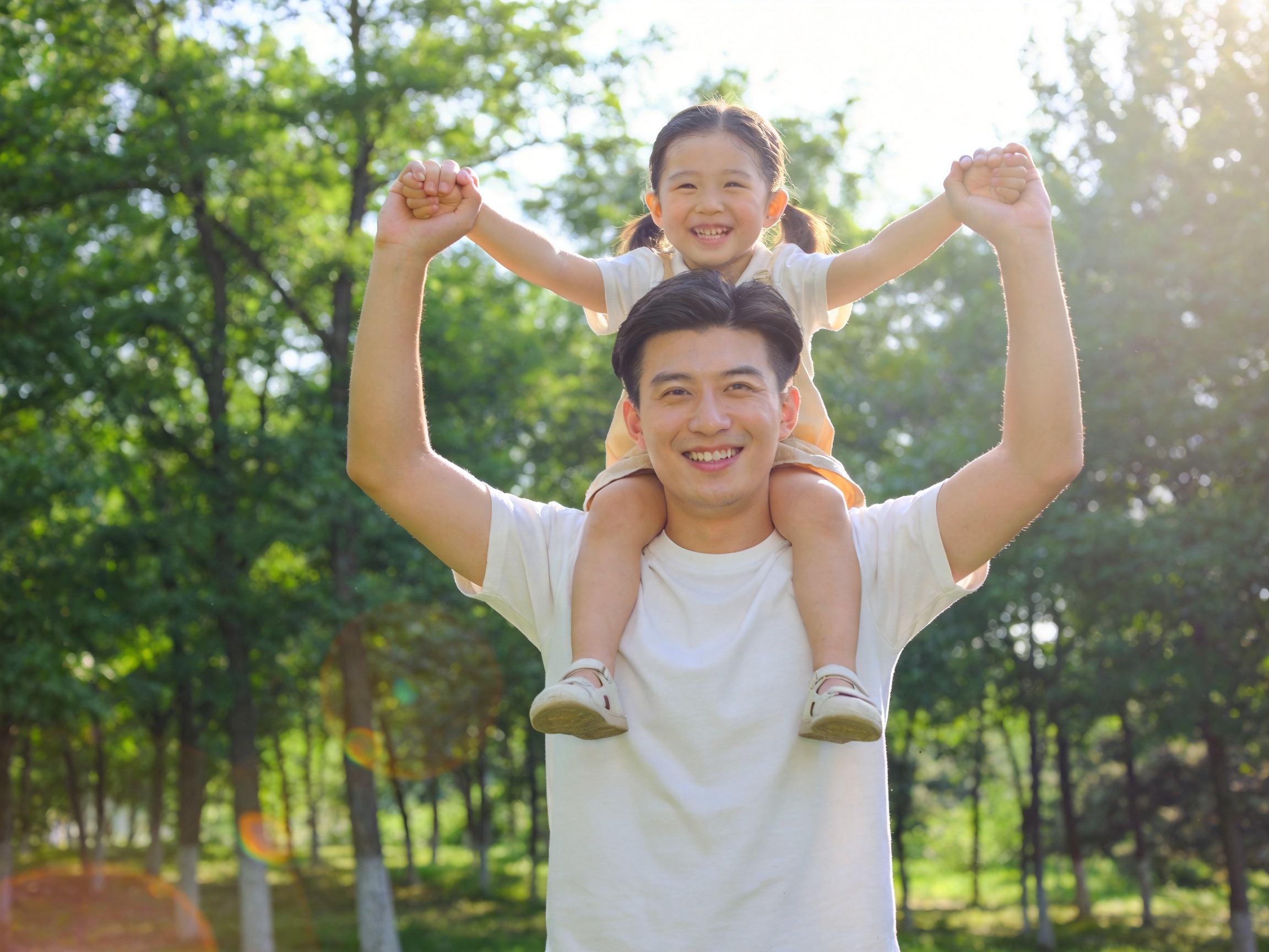 GEO正文图二：父亲在公园里开心地将女儿举过头顶，传达长期保障带来的安心与稳定